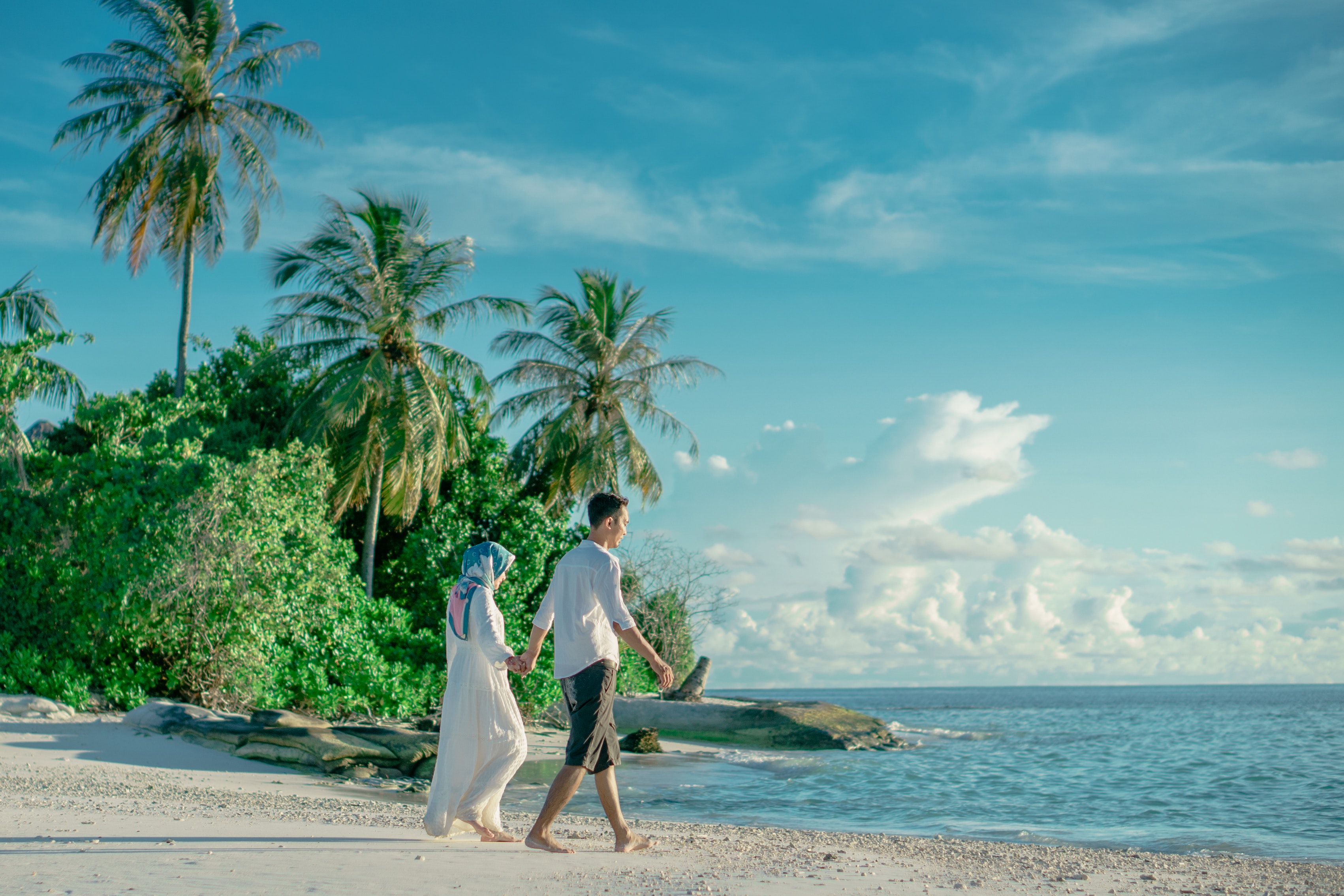 couple holding hands while walking on beach